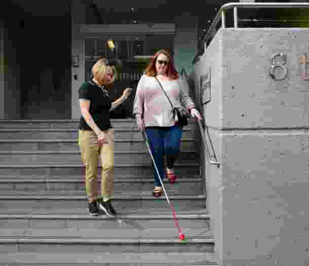 A person assisting a person using a white cane down a set of stairs.