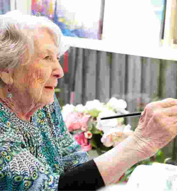 An older adult person painting with a paint brush.