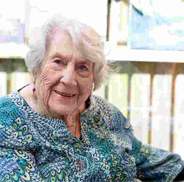 An older adult sitting in a chair smiling at the camera.