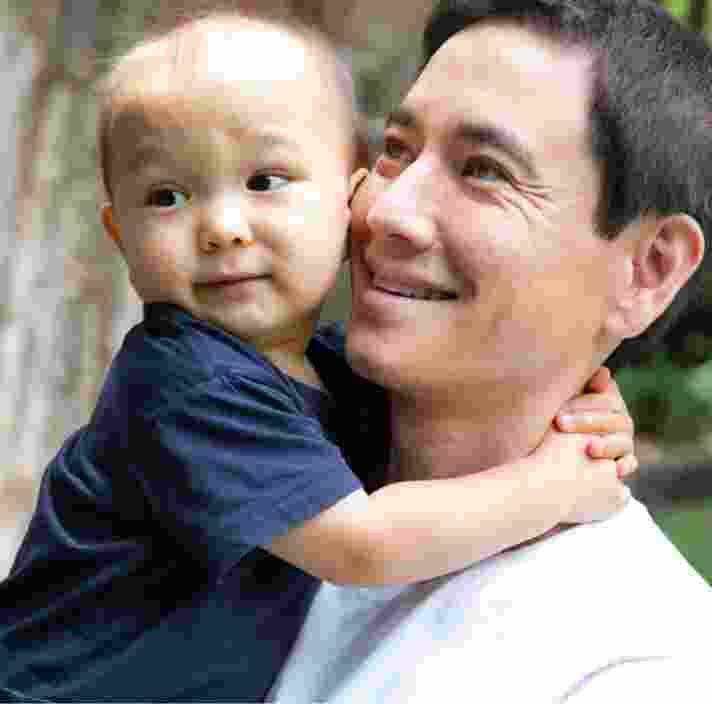 A father holding his toddler. The father has a smile on his face