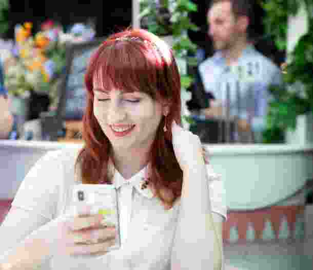 A person sitting at a cafe looking at their phone smiling.