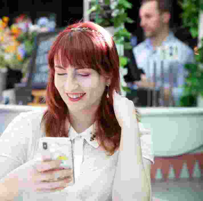 A person sitting at a cafe looking at their phone smiling.