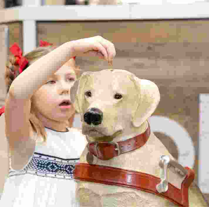 A young child putting a coin into a large Guide Dogs collection dog.