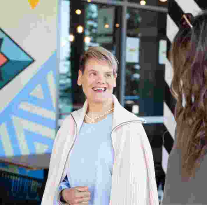 Two people looking at each other while they are walking down the street. One has their back to the camera while the other is smiling