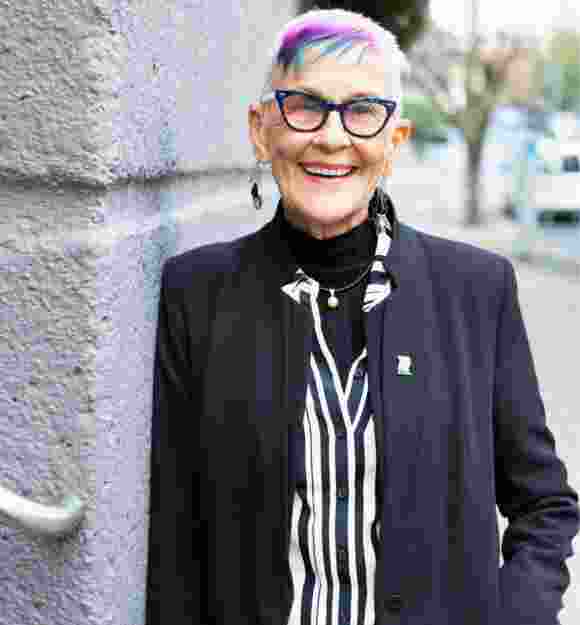 A person standing outside and leaning against a wall looking at the camera with a smile on their face.