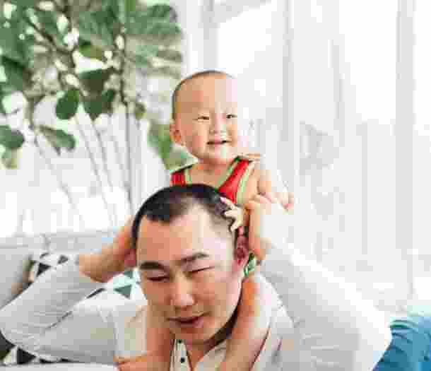 A man holding a baby on his shoulders inside a living room.