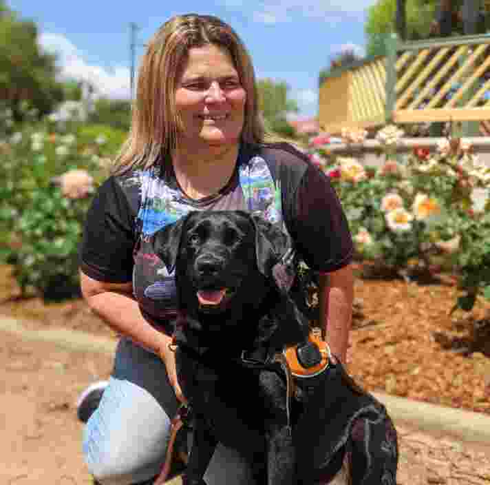 A woman crouches next to a black Labrador.