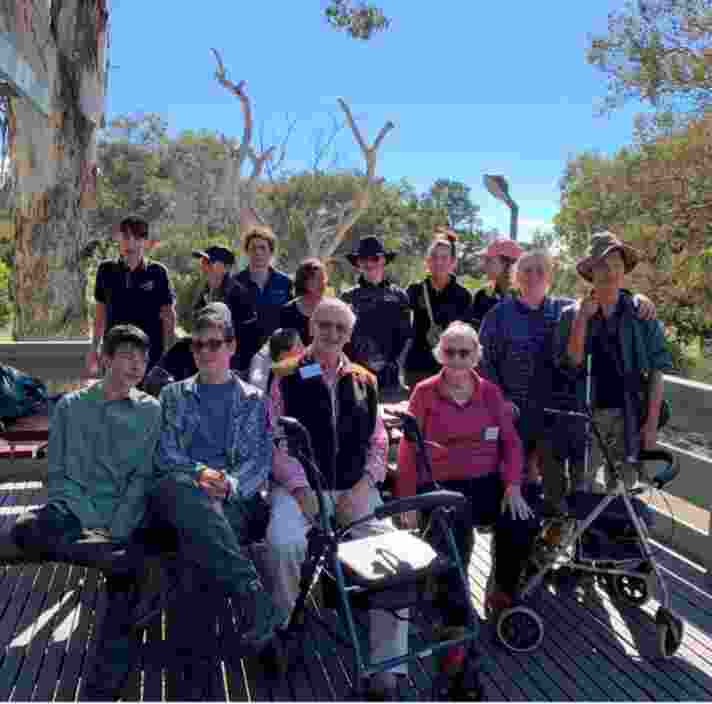 A group of people sitting on a deck with gum trees behind them.