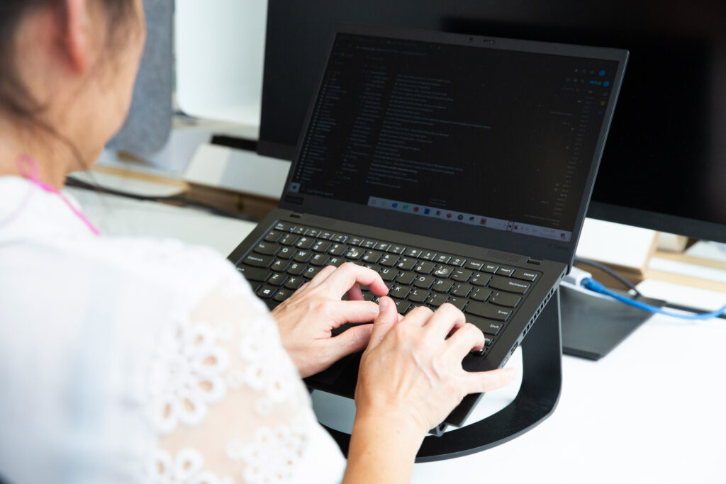 A woman wearing a white shirt typing on a laptop computer.