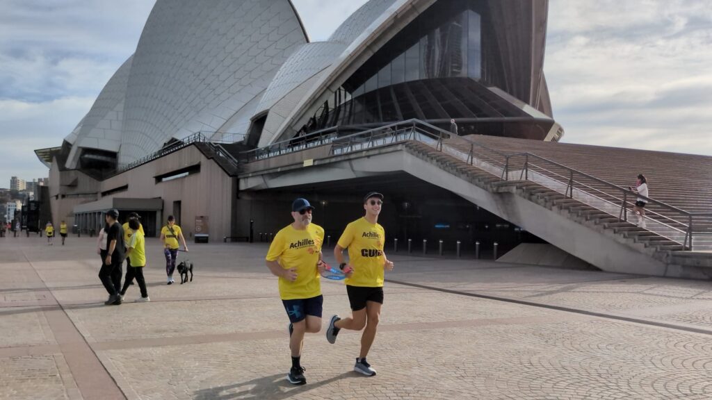 Two men run together next to the Sydney Opera House.