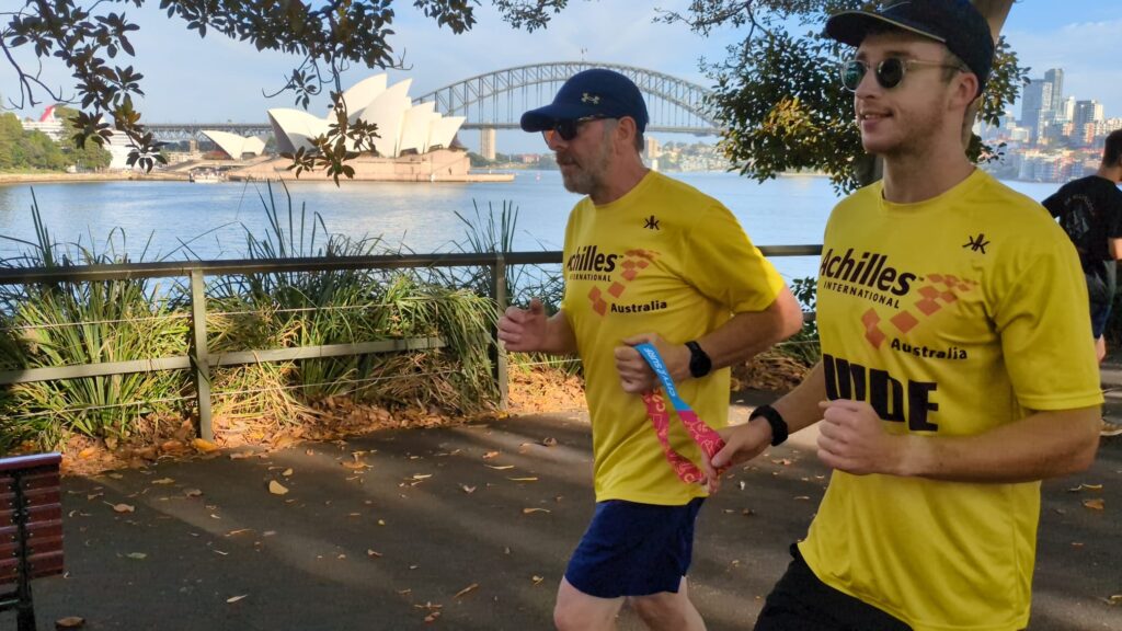 Two men run side by side along Sydney Harbour.