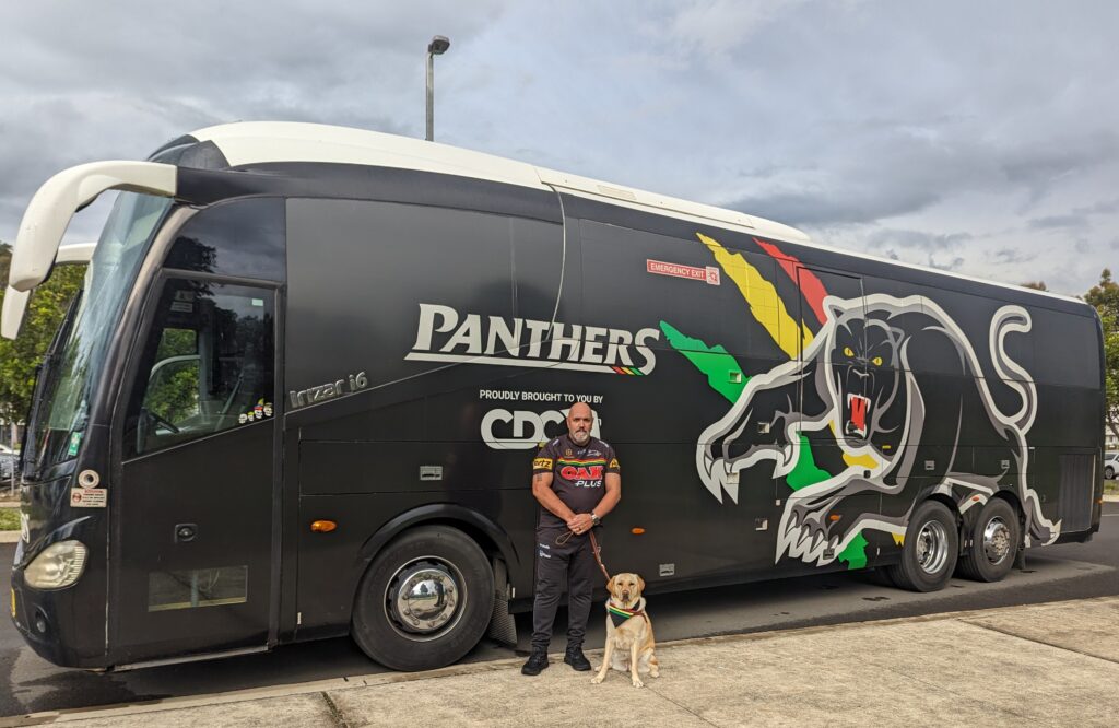 A man stands next to a bus with a yellow Labrador dog.