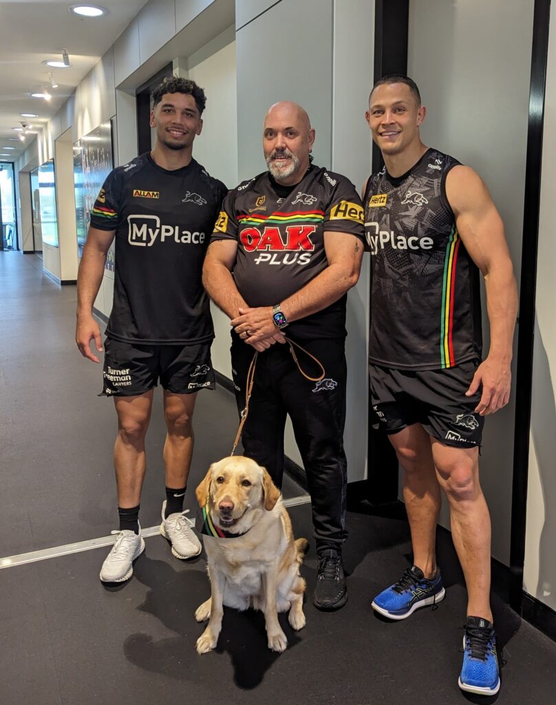 Two men pose together with a yellow Labrador dog.