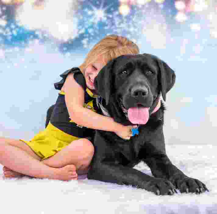 Ivy, a young girl, and Perry, a black Labrador, cuddling