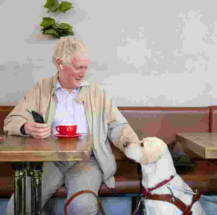 A person sitting at a cafe with their yellow Labrador.