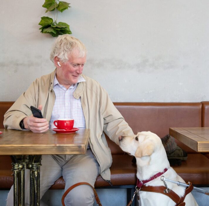 A person sitting at a cafe with their yellow Labrador.