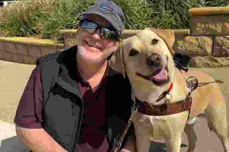 Tony and yellow Guide Dog Solo smiling at the camera.