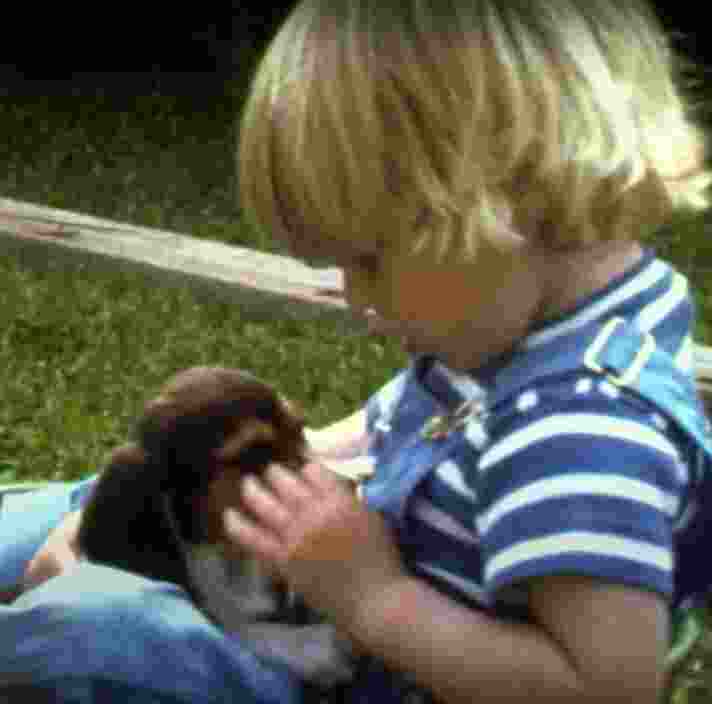A small child sitting outside on the grass holding a puppy