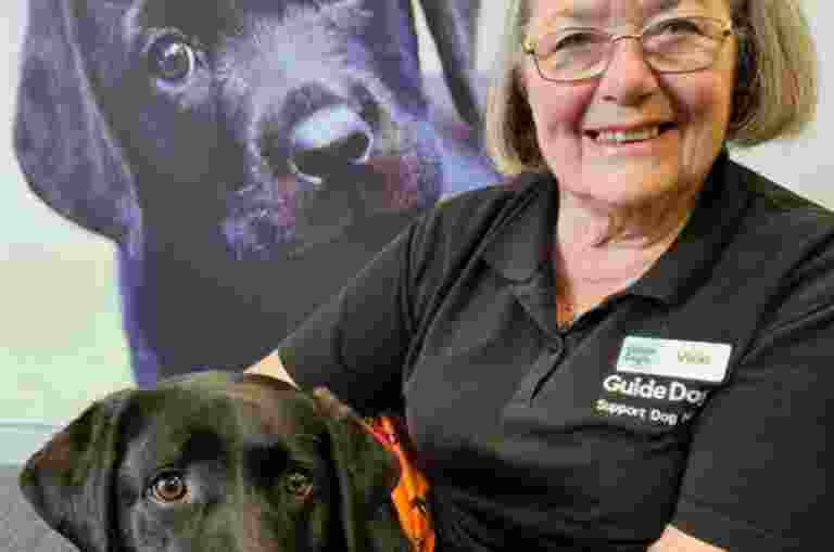 Vicki sitting next to a black Labrador.