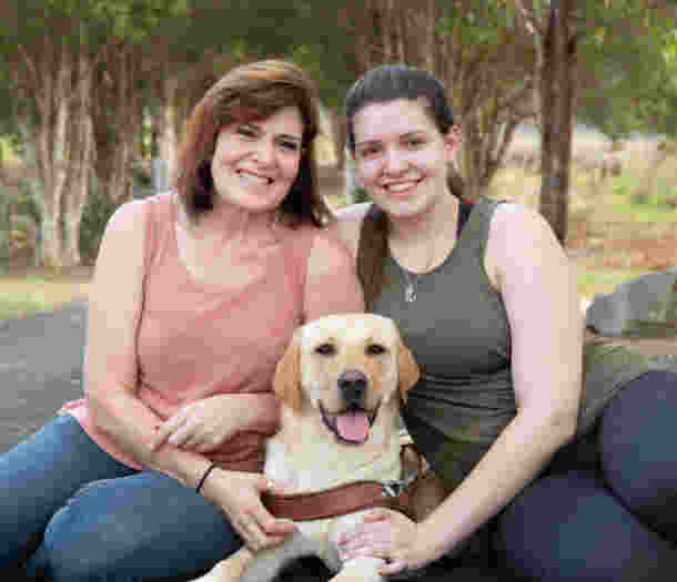 Two Puppy Raisers sitting either side of a yellow Labrador Guide Dog.