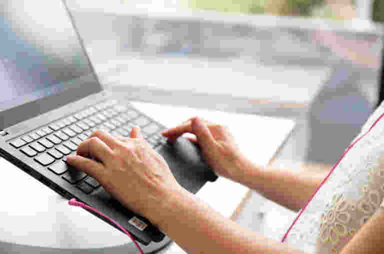 A close up of a womans hands typing on a laptop keyboard.