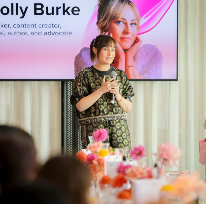Molly Burke stands in front of attendees at the Beauty Summit and speaks.