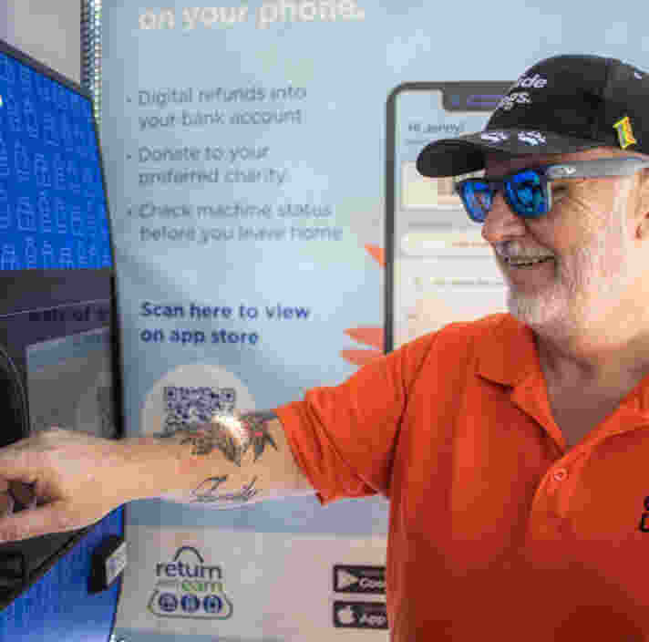 A man places a plastic bottle in a recycling machine.