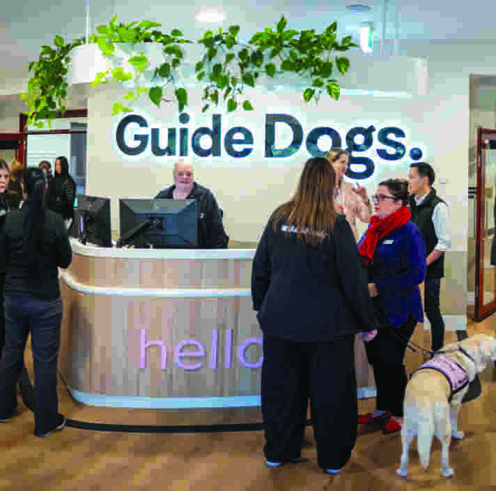 People standing around a reception space with a desk and a lit Guide Dogs sign.