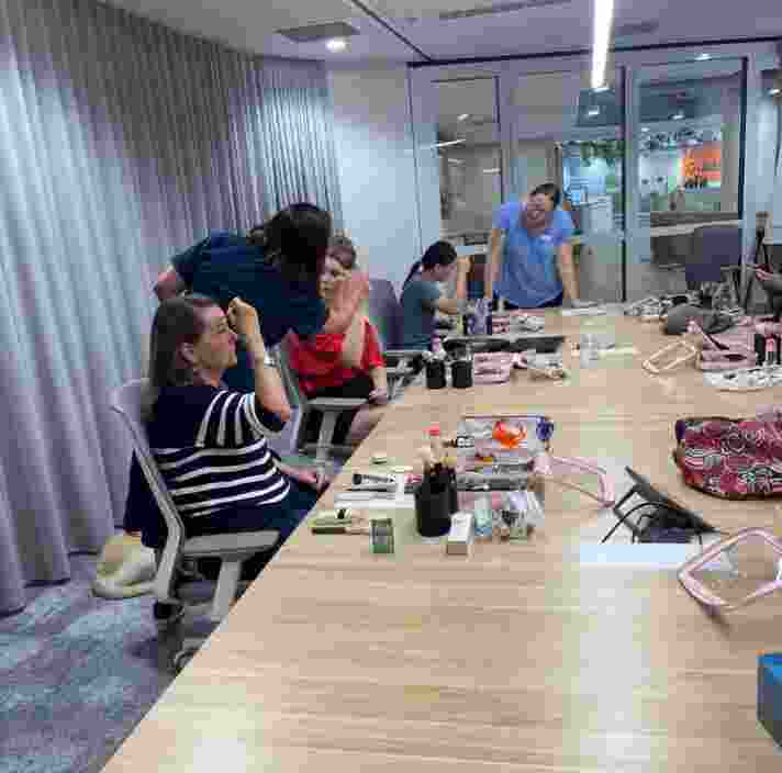 People seated at a boardroom table applying makeup.