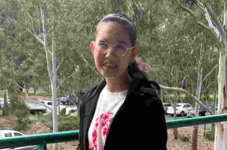 A young woman standing on a balcony with a white cane.
