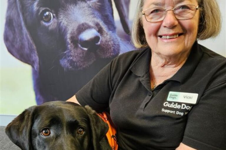 Vicki smiles at the camera holding a black Labrador.
