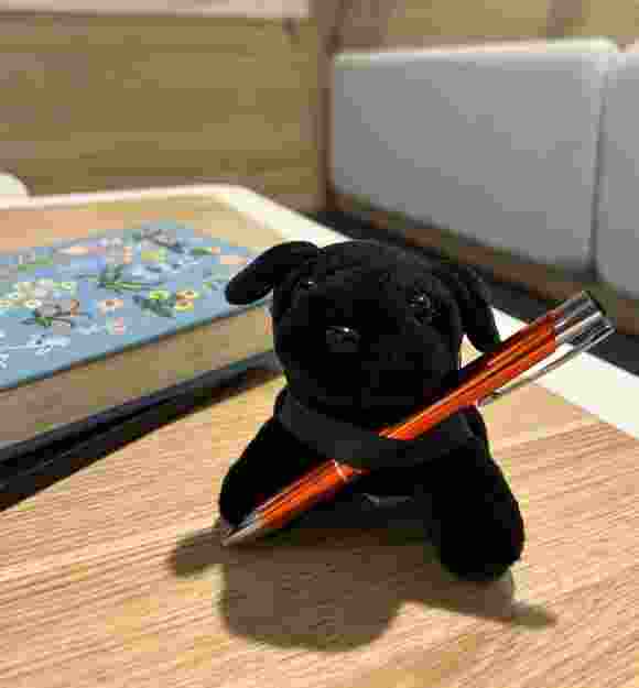 Black Labrador plush puppy with a pen.