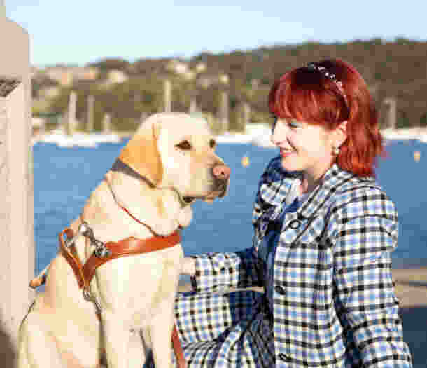 Yellow Labrador Guide Dog Banner sitting next to his Handler Ingrid on a pier.
