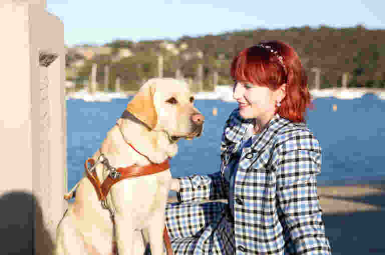 Yellow Labrador Guide Dog Banner sitting next to his Handler Ingrid on a pier.