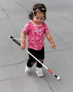 A young child walking with a white cane.