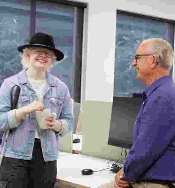 Two people standing and talking at a desk.