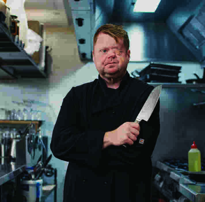 A man standing in a commercial kitchen holding a knife