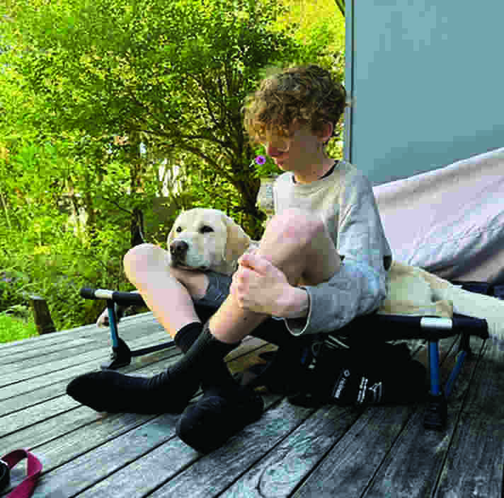 A boy sitting outside with a yellow Labrador resting its head on his knee.