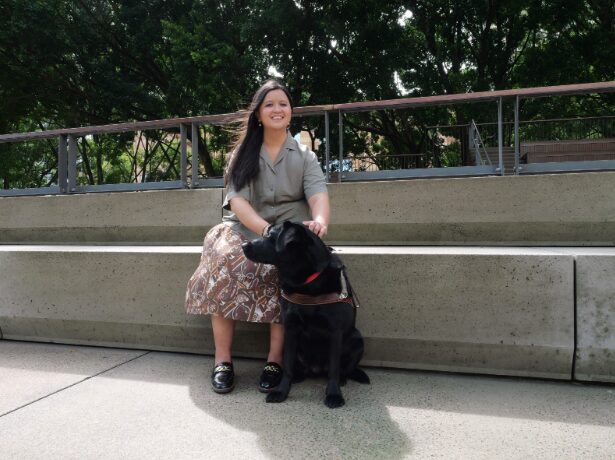 Ria and black labrador Guide Dog Trinity sitting down outsite