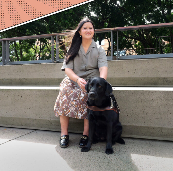 Ria and black Labrador guide dog sitting down outside.