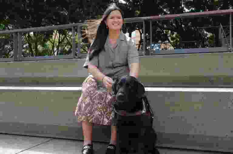 Ria and black Labrador guide dog sitting down outside.