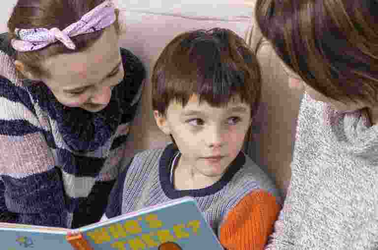 A young boy sits between his mother and his sister reading a book.