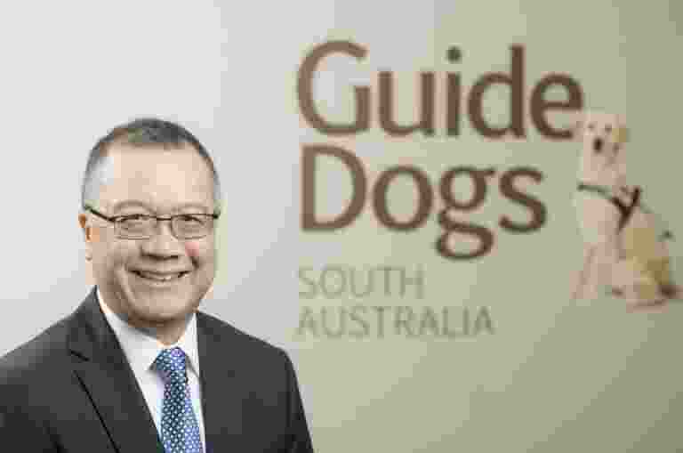 A smiling man standing in front of a Guide Dogs logo.