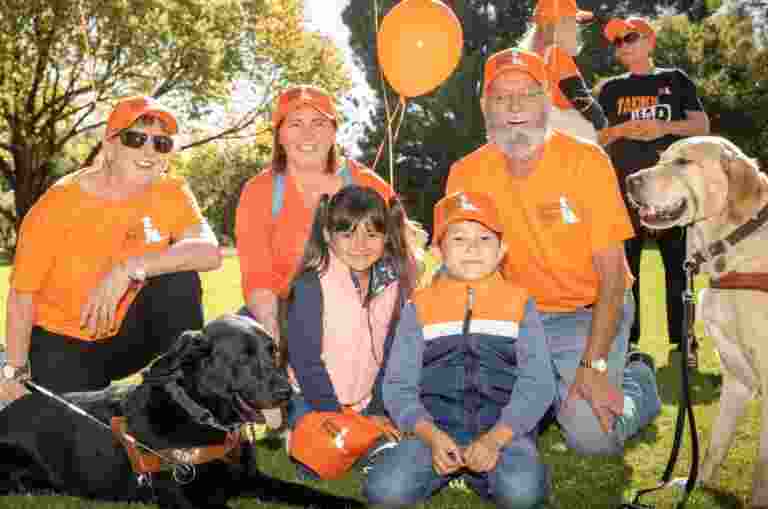 A group of Guide Dogs supporters and client gather outdoors to celebrate International Guide Dog Day.