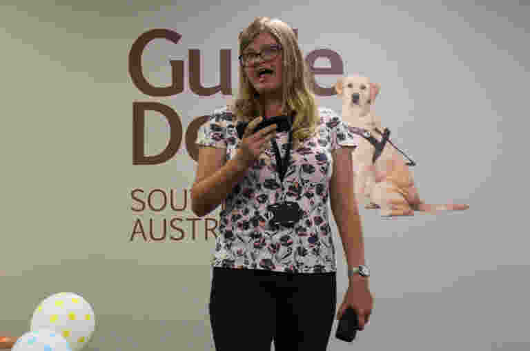 Woman standing in front of Guide Dogs logo, singing.