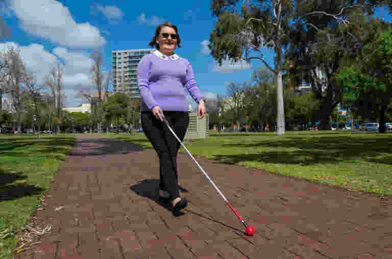 Woman with low vision outside walking and using her cane.