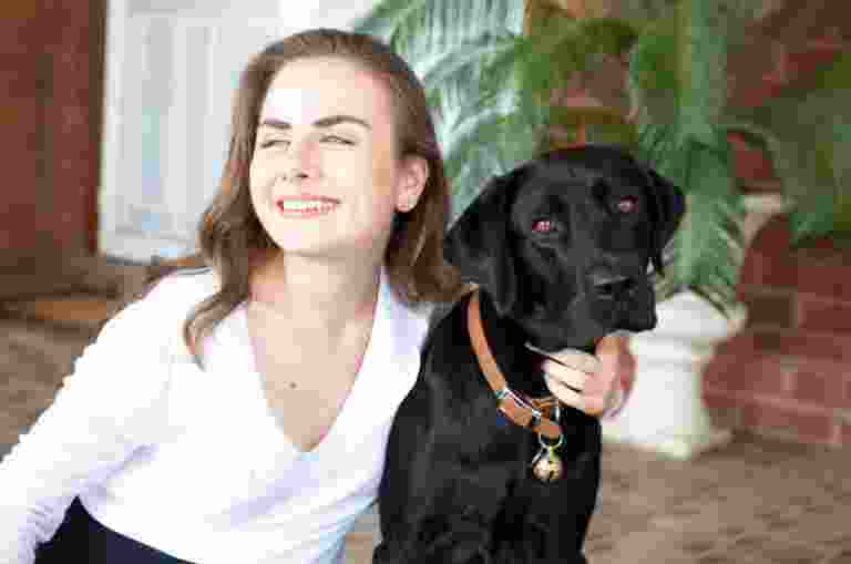 A young woman sits outside with her guide dog, looking off to the side.