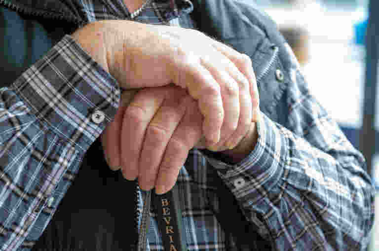 An older mans hands holding a white cane.