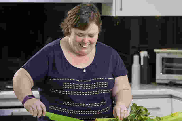 A woman with low vision is chopping celery at the kitchen bench.