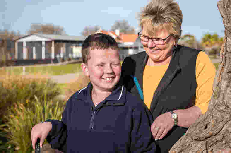 Ten-year-old Kodi and his mum Julie are standing in a park smiling.
